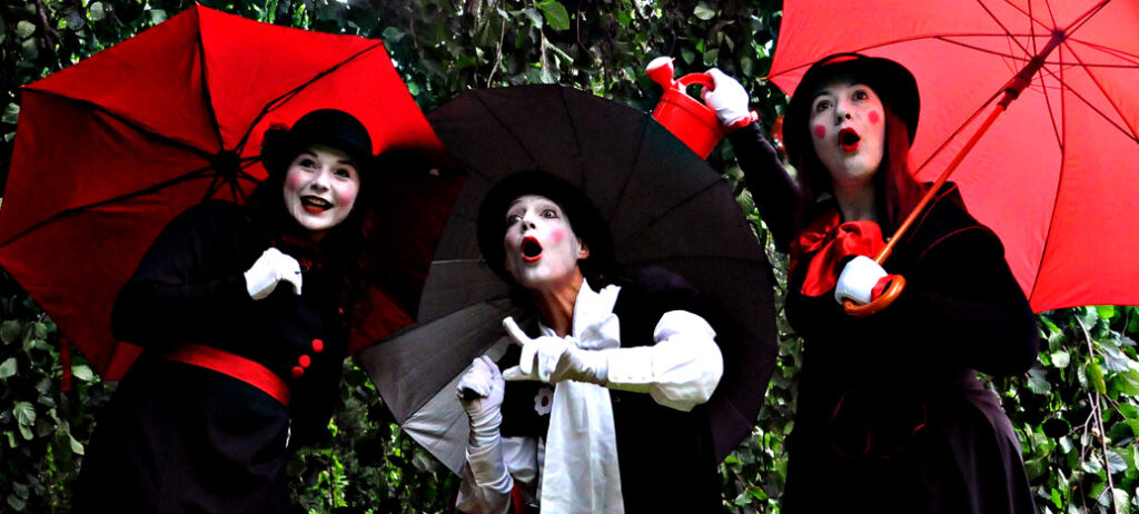 Drei Pantomime-Darstellerinnen mit roten und schwarzen Regenschirmen